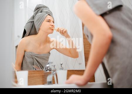 Frau mit einem Handtuch auf dem Kopf bürstet sich die Zähne. Stockfoto