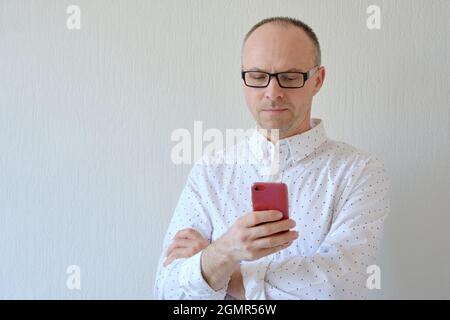 Porträt eines hübschen reifen Mannes mit einem Smartphone in der Hand, das vor einem weißen Hintergrund steht Stockfoto