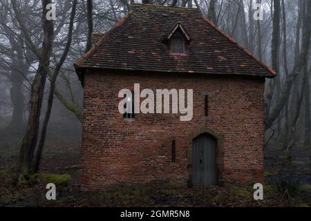 Dieses Fantasiebild eines gruseligen Hauses in einem nebligen Wald basiert auf dem Red Tower in York aus dem Jahr 1490. Stockfoto