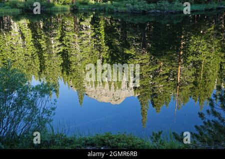 Spiegelung von Pinien und einem Granitgipfel in einem stillen Bergsee Stockfoto