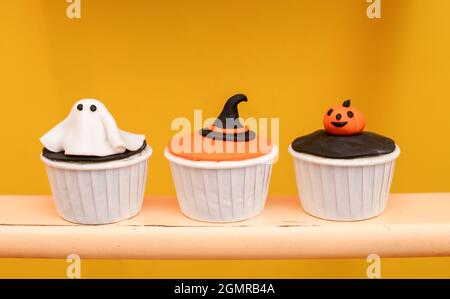 Halloween Muffins mit Dekorationen in Form von Geistern, Kürbissen und Hexenhüten. Ein Set festlicher Cupcakes und Leckereien für eine Halloween-Party. Stockfoto