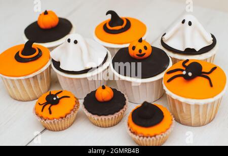 Halloween Muffins mit Dekorationen in Form von Geistern, Kürbissen und Hexenhüten. Ein Set festlicher Cupcakes und Leckereien für eine Halloween-Party. Stockfoto