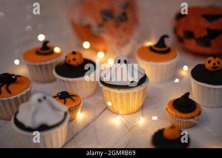 Halloween Muffins mit Dekorationen in Form von Geistern, Kürbissen und Hexenhüten. Ein Set festlicher Cupcakes und Leckereien für eine Halloween-Party. Stockfoto