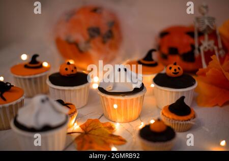 Halloween Muffins mit Dekorationen in Form von Geistern, Kürbissen und Hexenhüten. Ein Set festlicher Cupcakes und Leckereien für eine Halloween-Party. Stockfoto