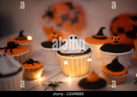 Halloween Muffins mit Dekorationen in Form von Geistern, Kürbissen und Hexenhüten. Ein Set festlicher Cupcakes und Leckereien für eine Halloween-Party. Stockfoto