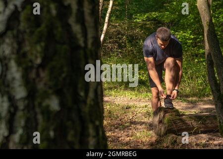 Der Sportler bindet die Schnürsenkel seiner Beine in Turnschuhen aus der Nähe der Sportler läuft im Park draußen, um den Wald, Eichen grünen Gras youn Stockfoto