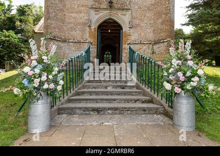 Blumenarrangements in Milchkichern vor einer Kirche an einem Hochzeitstag Stockfoto