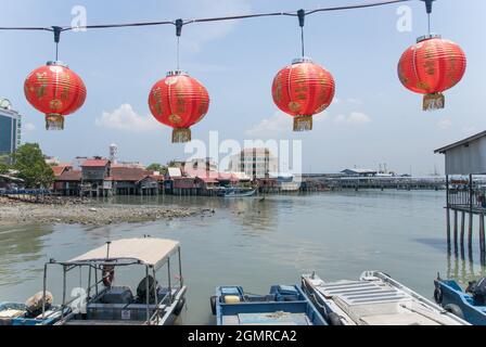 Rote Laternen hängen vor dem Meerblick mit Holzbooten und Häusern im Hintergrund in penang malaysia Stockfoto