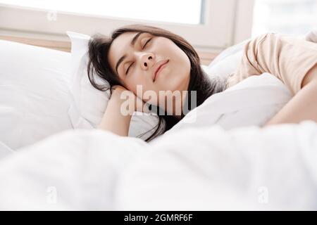 Nahaufnahme einer attraktiven lächelnden jungen Frau, die im Bett liegt Stockfoto