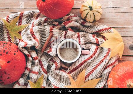 Tasse Kaffee Latte auf dem Tisch mit Kürbissen, gelben Blättern und Zimtstangen auf einem Strickpullover. Herbstkonzept, Draufsicht. Flach liegend Stockfoto