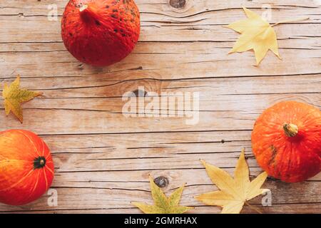 Draufsicht auf Hokkaido-Kürbisse und Herbstblätter auf Holztisch. Flach liegend, Kopierplatz Stockfoto