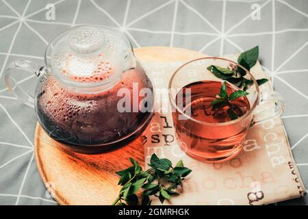 Eine Tasse Kräutertee und Wasserkocher auf einem Holztablett auf dem Bett. Gemütlicher Herbst. Frühstück im Zimmer. Draufsicht Stockfoto