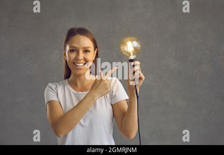 Glückliche schöne Frau hält Glühbirne schlägt gute Idee und intelligente Lösung des Problems Stockfoto