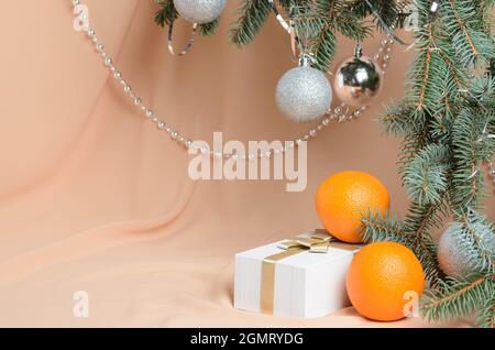 Weihnachten. Eine Neujahrskomposition aus Zweigen eines Weihnachtsbaums, verziert mit silbernen Kugeln, einer Geschenkbox, orange auf einem Hintergrund mit Fleisch-Co Stockfoto