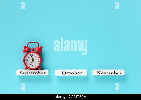 Holzkalender Herbstmonate und roter Wecker über September auf blauem Hintergrund. Konzept September Zeit Kreativ Draufsicht Flat Lay Minimal Stil C Stockfoto