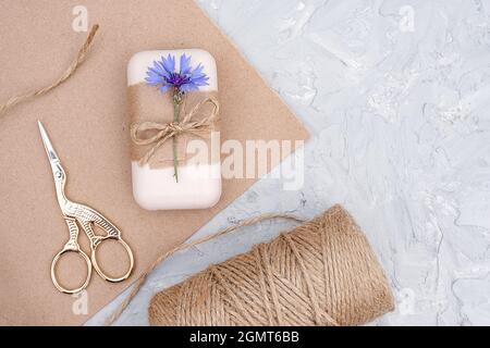 Verpackung von natürlicher handgemachter Seife, dekoriertes Kraftpapier, blaue Blume, Garnklee und Schere. Konzept der Bio-Kosmetik. Draufsicht Flat Lay Stockfoto