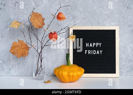 Happy Friday Text auf schwarzem Briefbrett und Strauß von Zweigen mit gelben Blättern auf Wäscheklammern in Vase auf Tisch Vorlage für Postkarte, Gruß Auto Stockfoto