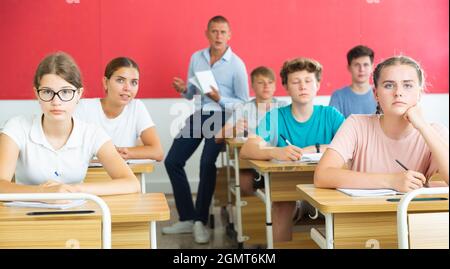 Jugendliche hören dem Dozenten zu und schreiben in Notizbüchern im Klassenzimmer Stockfoto