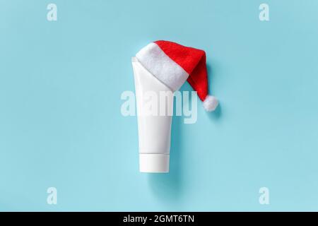 Kosmetische, medizinische weiße Tube für Creme, Salbe oder anderes Produkt in rotem Weihnachtsmann Hut auf blauem Hintergrund. Konzept Winter Haut-und Körperpflege oder Weihnachten Stockfoto