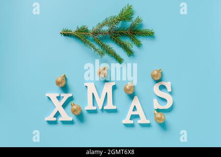 Urlaubsgestaltung. Text Weihnachten aus weißen Buchstaben, grünen Tannenzweig und weihnachtsdekoration goldene Kugeln auf blauem Hintergrund. Concept frohe weihnachten. Stockfoto