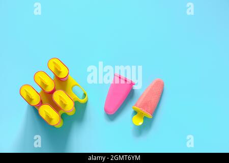 Hausgemachte Fruchtknöchel. Natürliches Erdbeereis in hellen Plastikformen auf blauem Hintergrund mit Kopierraum. Draufsicht Flat Lay Template für Ihr. Stockfoto