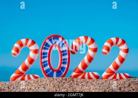 Kreative Neujahrs- und Weihnachtskarte.die hellen Neujahrszahlen 2022 in Streifen, am Strand am Meer, vor dem Hintergrund des blauen Himmels.Nahaufnahme. Stockfoto