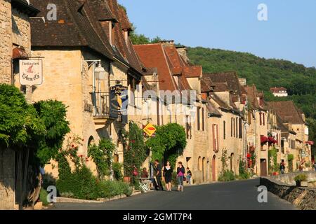 Traditionelle Steinbauten entlang der Dordogne, die kurz vor Sonnenuntergang in La Roque Gageac, Perigord, Aquitanien, Frankreich, Gold glühen Stockfoto