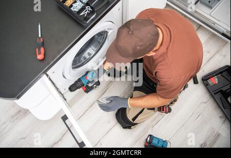 Professioneller kaukasischer Tischler in seinen 40er Jahren Finishing Washer Cabinet in Clients Apartment. Stockfoto