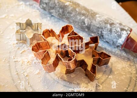 Schneeflocken-förmige Kupfer-Metall-Keks schneiden auf einer bemehlten Oberfläche neben einem Nudelholz. Stockfoto