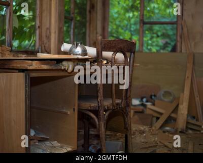 Leerer Raum des verlassenen Hauses, ein Holzstuhl und ein Tisch stehen im Zentrum der Komposition Stockfoto