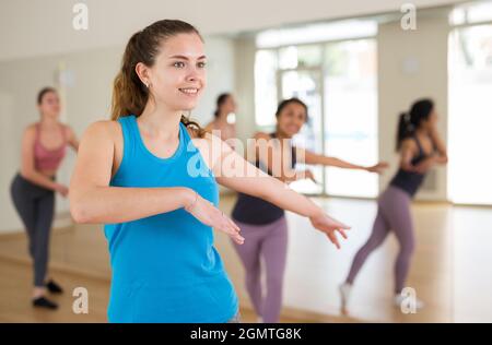 Portrait eines lächelnden tanzenden Mädchens, das während des Gruppentrainings im Tanzstudio kräftigen Schwung übt. Stockfoto