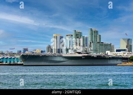 Die USS Midway, das historische Schlachtschiff des Flugzeugträgers, das heute ein Museum ist, befindet sich im Hafen von San Diego mit der Skyline der Innenstadt von San Diego im Hintergrund Stockfoto