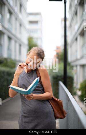 Ein vielbeschäftigter persönlicher Assistent ruft am Telefon an und nimmt gleichzeitig Notizen auf, während er auf der Stadtstraße läuft Stockfoto