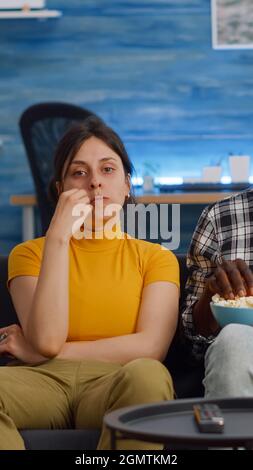 POV von interracial paar Film im Fernsehen mit Snack zu Hause. Verheiratete multiethnische Liebhaber, die beim Essen von Popcorn im Wohnzimmer auf die Kamera schauten. Gemischte Rassen Menschen kleben auf dem Sofa Stockfoto