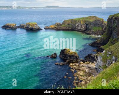 Die Küste der Grafschaft Antrim in Nordirland ist sowohl spektakulär als auch wunderschön und wird von steilen Klippen, smaragdgrünem Wasser, Höhlen und der winzigen, vor der Küste gelegenen isla geziert Stockfoto