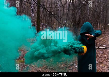 Eine gruselige Hexe hält einen dampfenden Kürbis in einen tiefen Wald. Jack o Laterne mit grünem Rauch für halloween Stockfoto