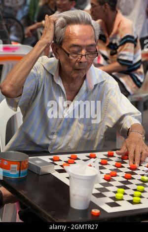 Chinatown, Singapur - 1. April 2011; mehrere alte Männer im Blick. Dieser rauchende Mann bleibt völlig konzentriert auf sein Spiel der Dame in diesem lauten, offenen aufgehört Stockfoto