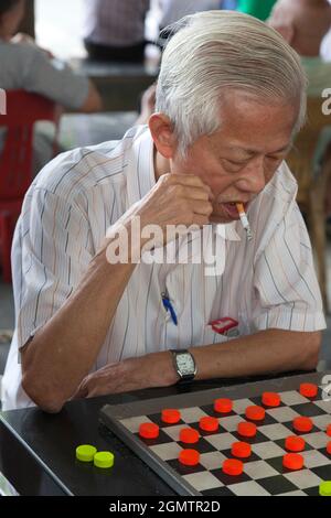 Chinatown, Singapur - 2. April 2011; mehrere alte Männer im Blick. Dieser rauchende Mann bleibt völlig konzentriert auf sein Spiel der Dame in diesem lauten, offenen aufgehört Stockfoto