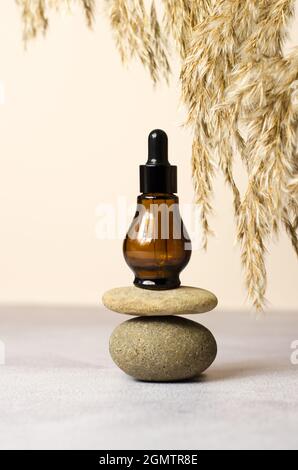 Eine braune Kosmetikflasche auf einem Podium aus Natursteinen und ein Rahmen aus Schilfzweigen. Natürliche Bio-Kosmetik, Mockup Stockfoto