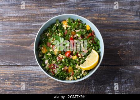 Original orientalischer Salat Tabbouleh mit Kohlkalk, Petersilie, Bulgur, Tomaten und roten Zwiebeln auf einem Holztisch, Draufsicht. Gesunde hausgemachte Speisen Stockfoto