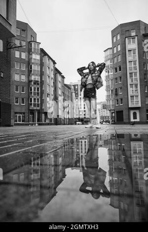 Mädchen in der Nähe Herbst Pfütze mit Reflexionen auf dem Stadtplatz Stockfoto