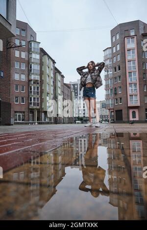 Mädchen in der Nähe Herbst Pfütze mit Reflexionen auf dem Stadtplatz Stockfoto