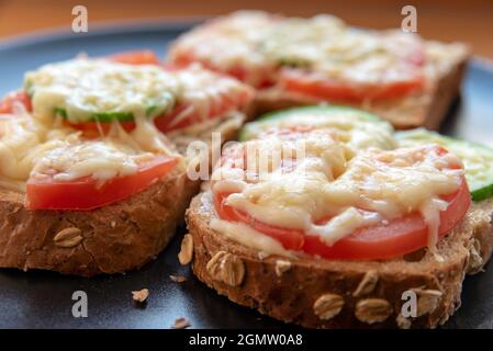 Heiße Sandwiches mit Mayonnaise, Tomaten, Gurken und geriebenem Käse auf einem schwarzen Teller Stockfoto