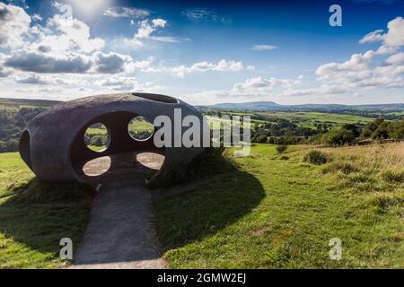 Design von Peter Meacock mit Katarina Novomestska und Architecture Central Workshop. Pendle's Panopticon, 'Atom', liegt auf dem Hügel über dem Dorf Wycoller im Wycoller Country Park. Sie besteht aus Ferrozement mit einer Oberflächenbeschichtung auf Metallbasis und ist sowohl ein beeindruckender moderner Aussichtspunkt als auch ein Zufluchtsort, von dem aus Sie die herrliche Landschaft von Pendle genießen können, als auch ein faszinierendes und schönes Objekt, das von weitem betrachtet werden kann. Von innen bieten die kreisförmigen Aussichtsräume einen spektakulären Blick auf die umliegende Landschaft. Wycoller ist eine historische Siedlung, die über 1000 v. Chr. hinausgeht. Stockfoto