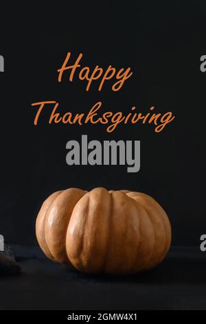 Orange großer Kürbis auf schwarzem Hintergrund. Text - Happy Thanksgiving. Vorderansicht. Vertikales Format. Stockfoto