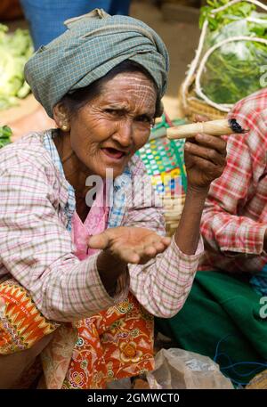 Alte Stammesfrau, mit Thanaka-Make-up, raucht eine unverschämte, selbst angebaute und handgerollte Zigarre in Nyaung - U Market in Mandalay, Myanmar.Verdampfen ist Clea Stockfoto