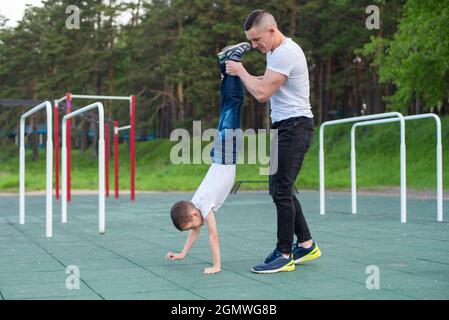 Kaukasischer Mann lehrt Sohn Handstand auf Spielplatz. Stockfoto
