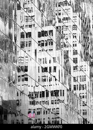 New York, USA - 4. November 3023 verzerrte Spiegelungen von Wolkenkratzern hüpfen um diesen archetypischen Street Canyon in Manhattan. Dazu eine einsame US-Flagge.4 Stockfoto