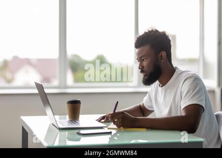 Fokussierter afroamerikanischer Geschäftsmann, der mit Laptop-Dokumenten in Bürodokumenten arbeitet, die Berichte vorbereiten und Arbeitsergebnisse analysieren, schwarze männliche Analysen Stockfoto