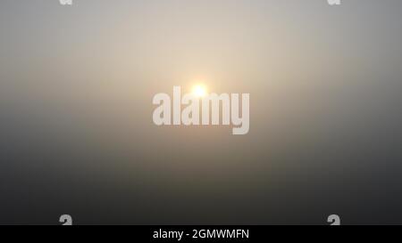 Blick auf den Sonnenaufgang am Morgen durch dichten Nebel. Herbstwetter mit Nebel Stockfoto